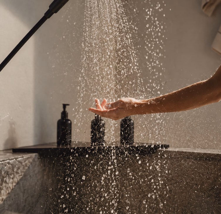 Hand under the shower spray above a shelf with bottles
